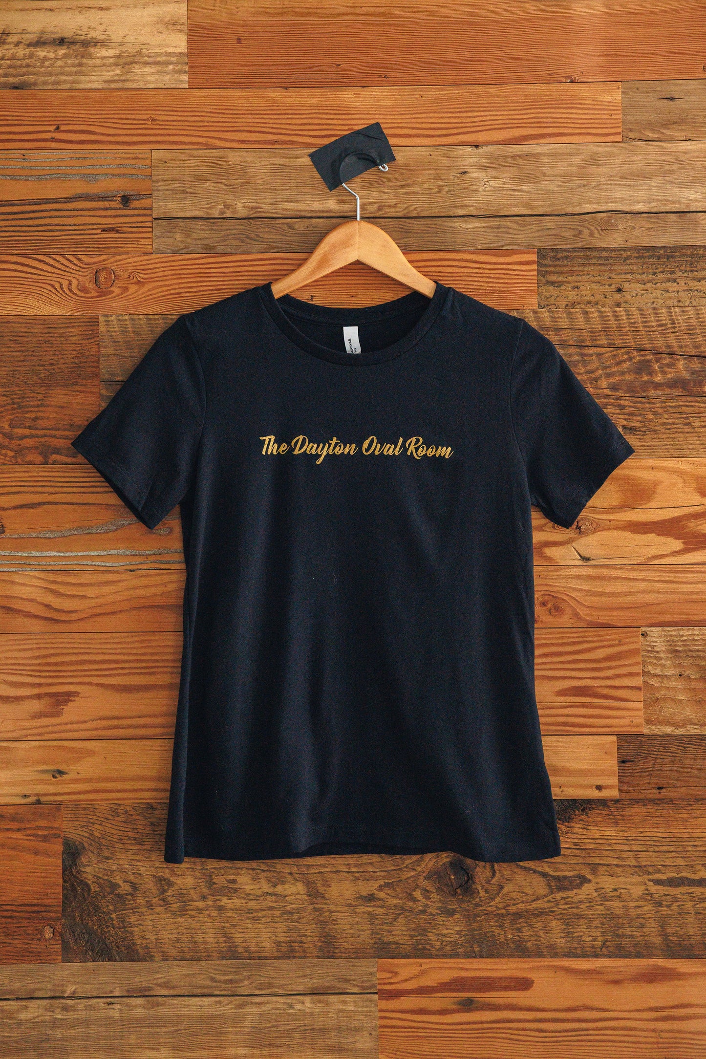 Black t-shirt with gold text on a wooden background