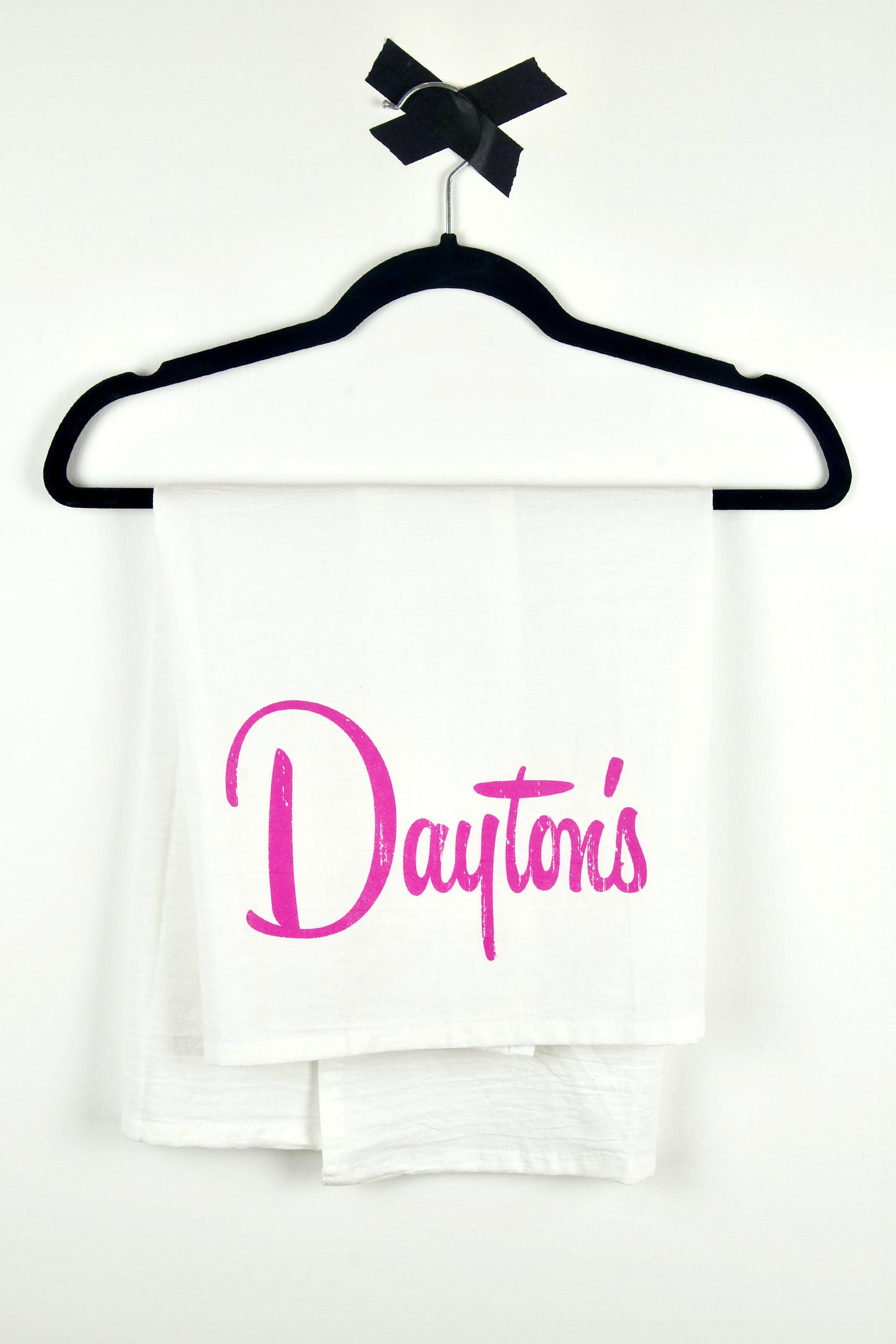 White flour sack towel with 'Dayton's' printed in pink on a black hanger against a white background