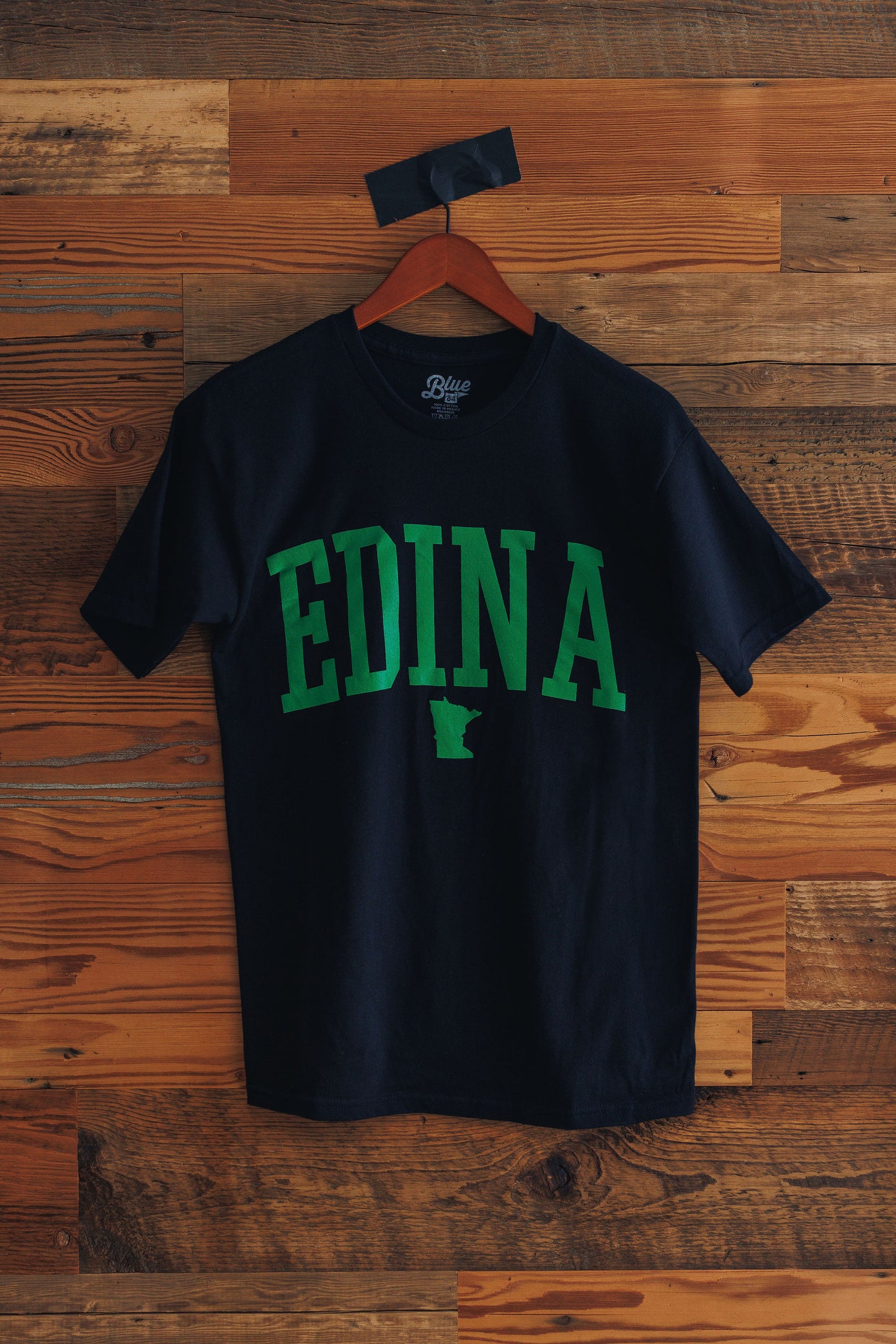 Black t-shirt with 'EDINA' printed in green on a wooden background