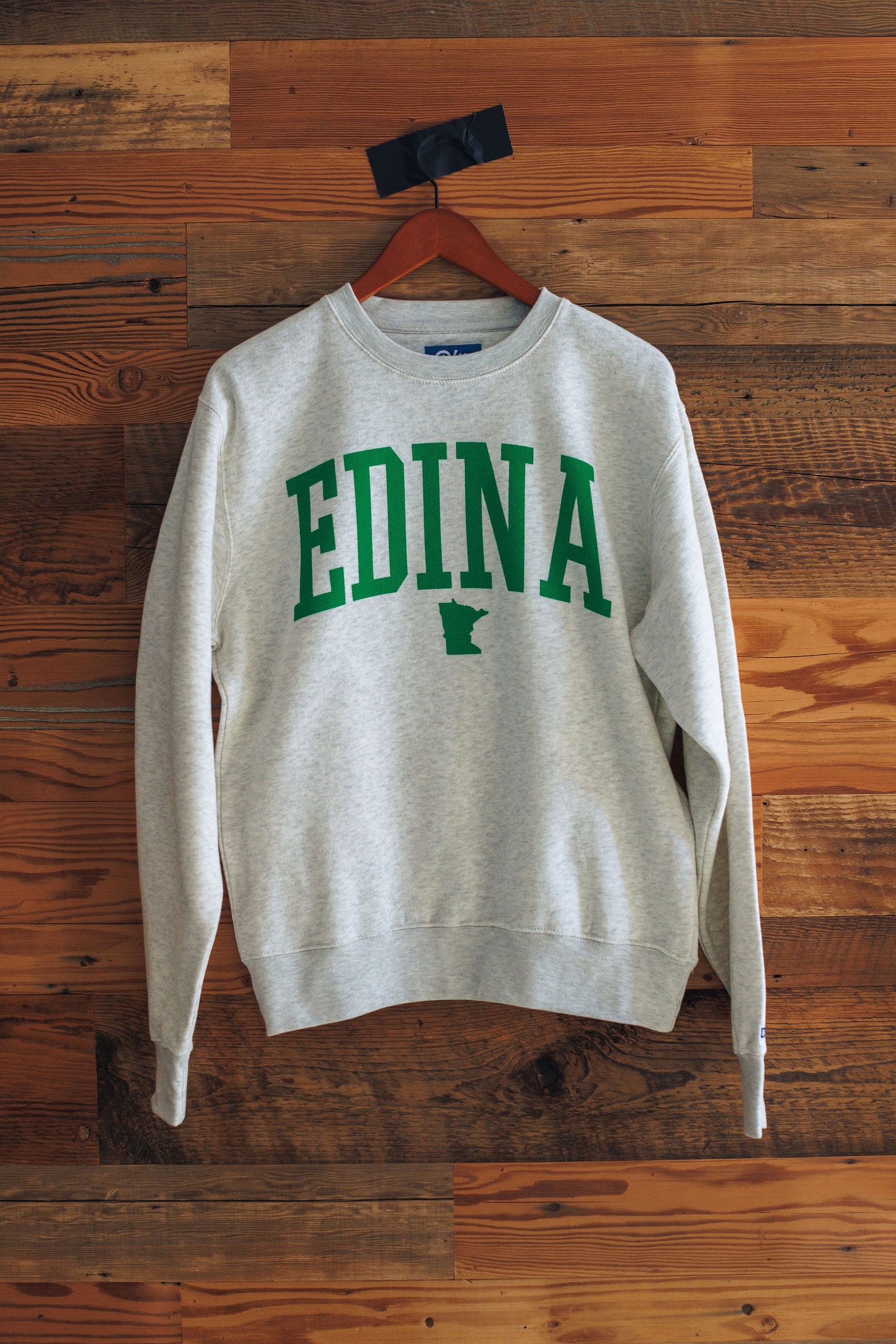 Gray sweatshirt with 'EDINA' printed in green on a wooden background