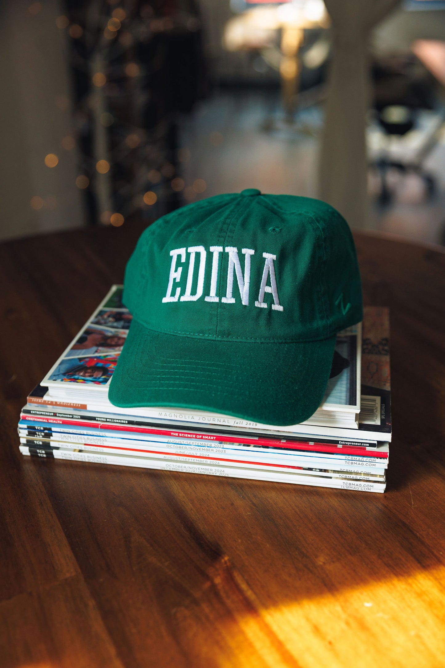 Green cap with 'EDINA' text on a stack of magazines on a wooden table