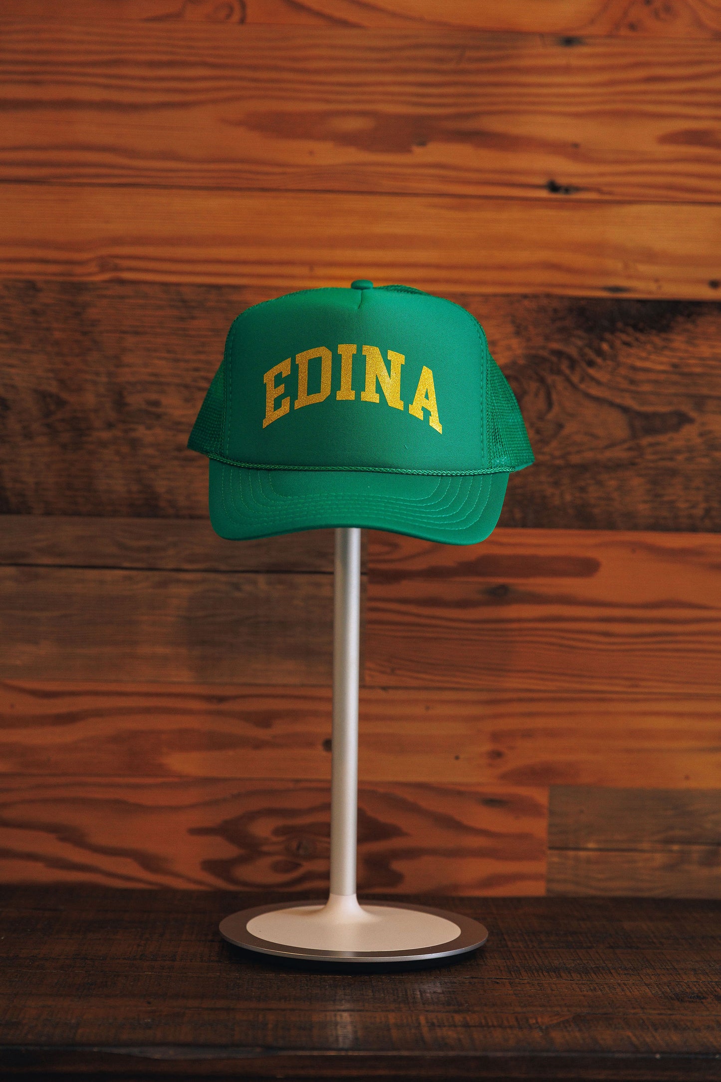 Green cap with 'EDINA' text on a stand against a wooden background