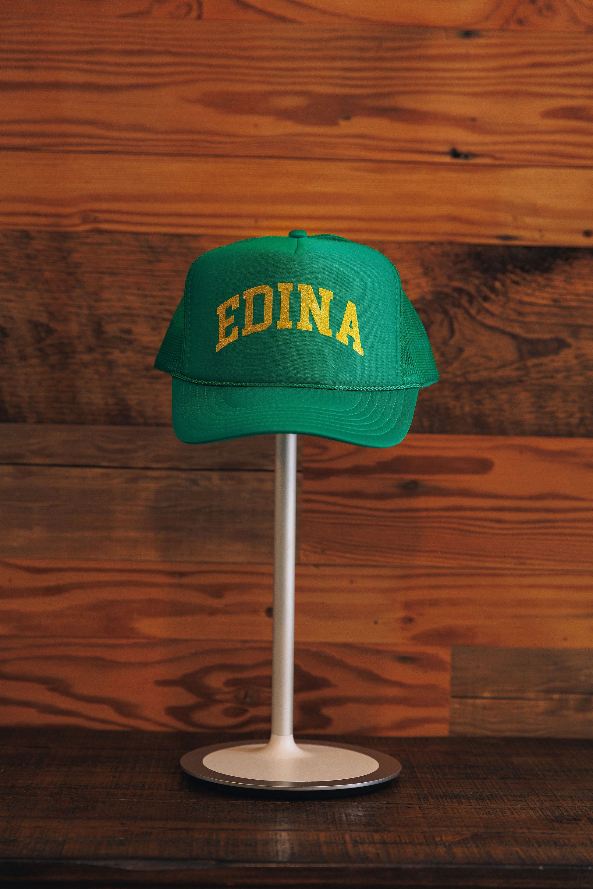 Green cap with 'EDINA' text on a stand against a wooden background