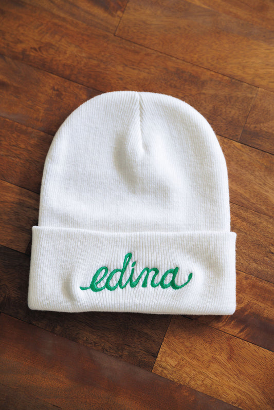 White beanie with 'edina' embroidery on a wooden surface