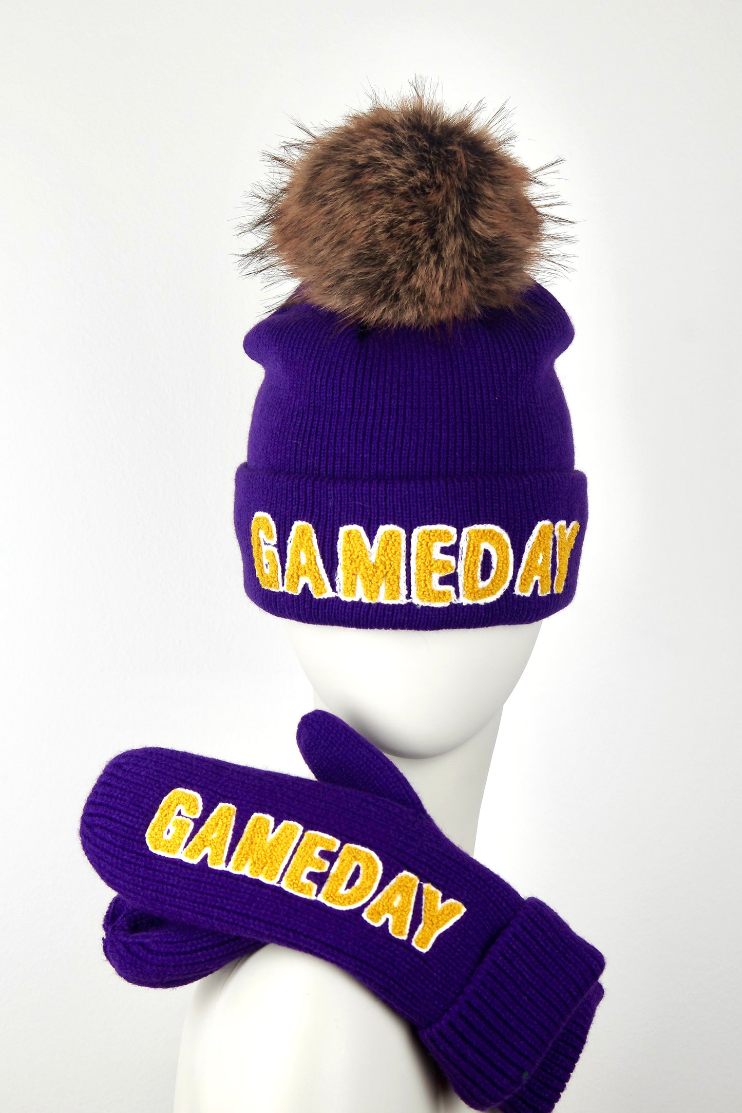 Purple 'GAMEDAY' beanie with fur pom-pom and matching gloves on a mannequin head against a white background.