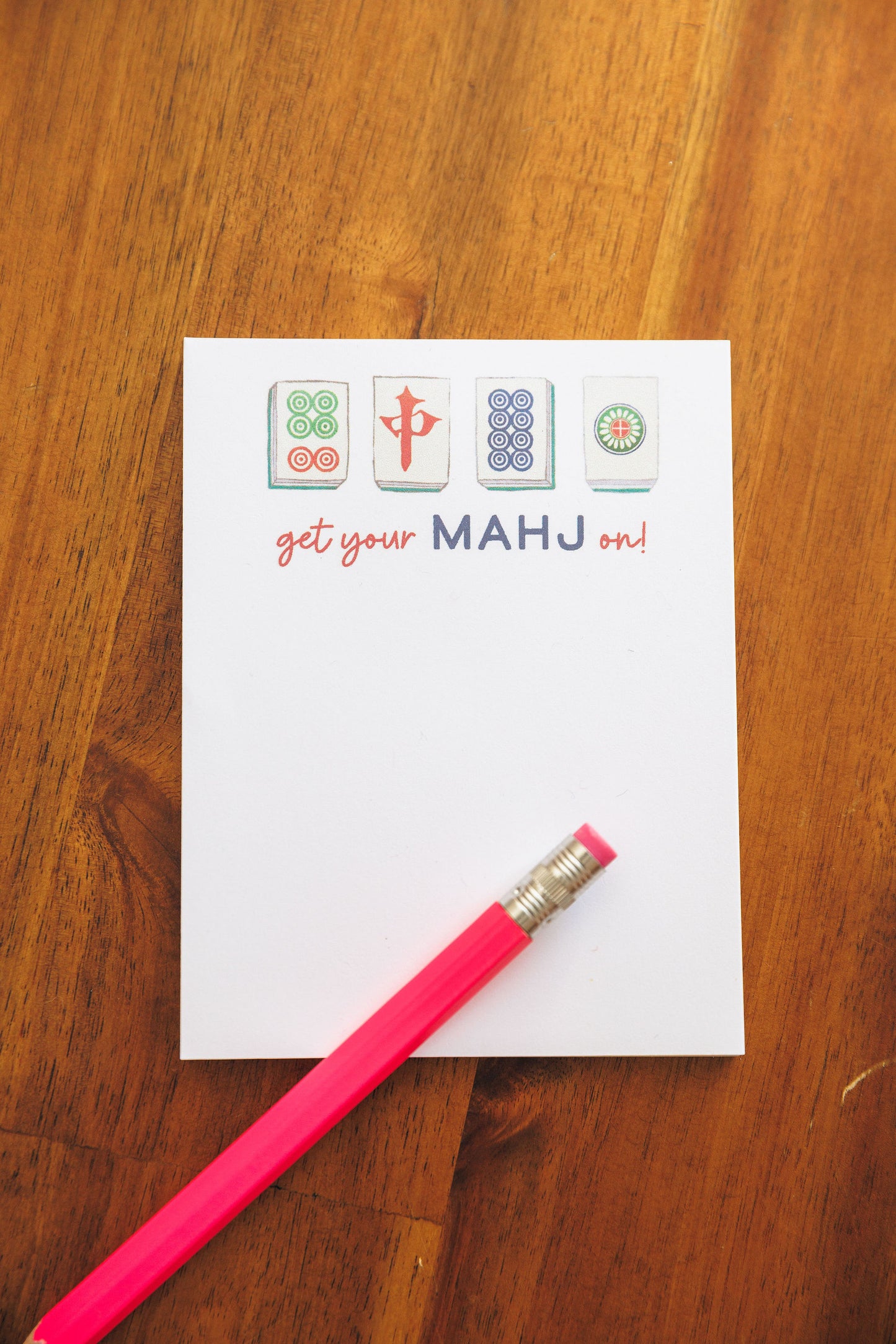 Notepad with colorful icons and text on a wooden surface with a pink pencil.