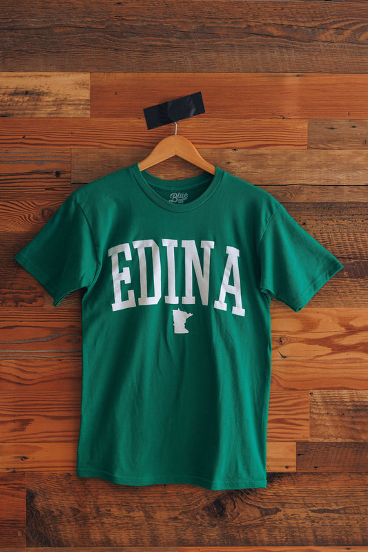 Green t-shirt with 'Edina' and a state outline on a wooden background