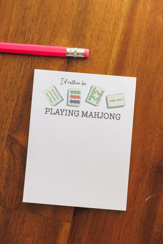 Note with 'I'd rather be playing Mahjong' text on a wooden surface with a pink pencil.