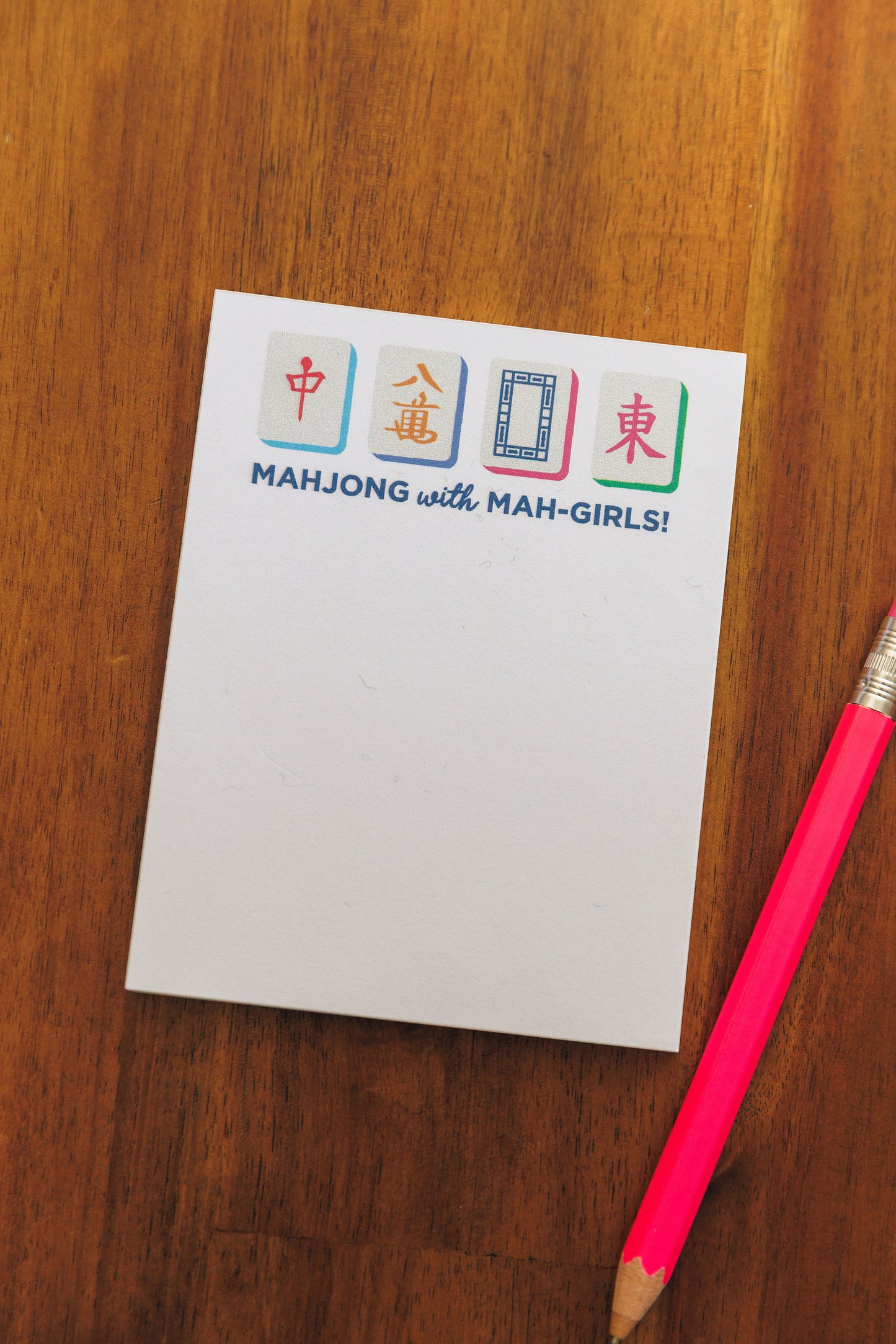 Notepad with 'Mahjong with Mah-Girls!' design on a wooden surface with a pink pencil.