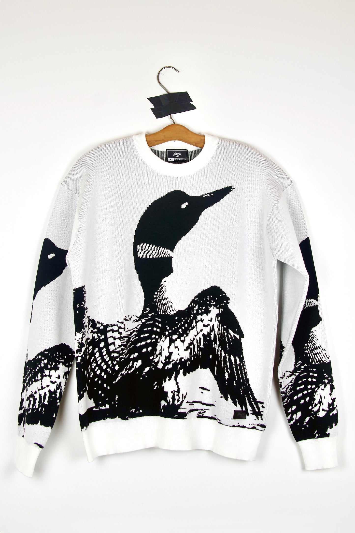 White sweater with loon design on a hanger against a white background
