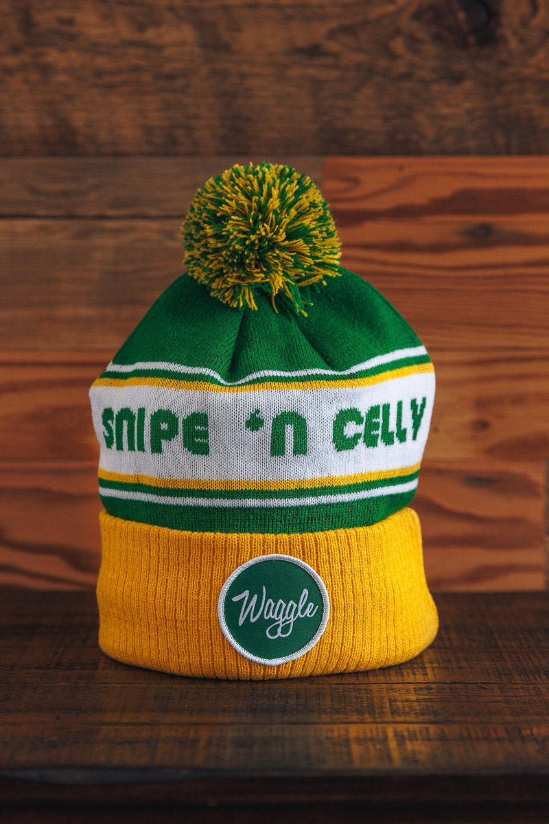 Knitted beanie with green and yellow pom-pom on a wooden surface