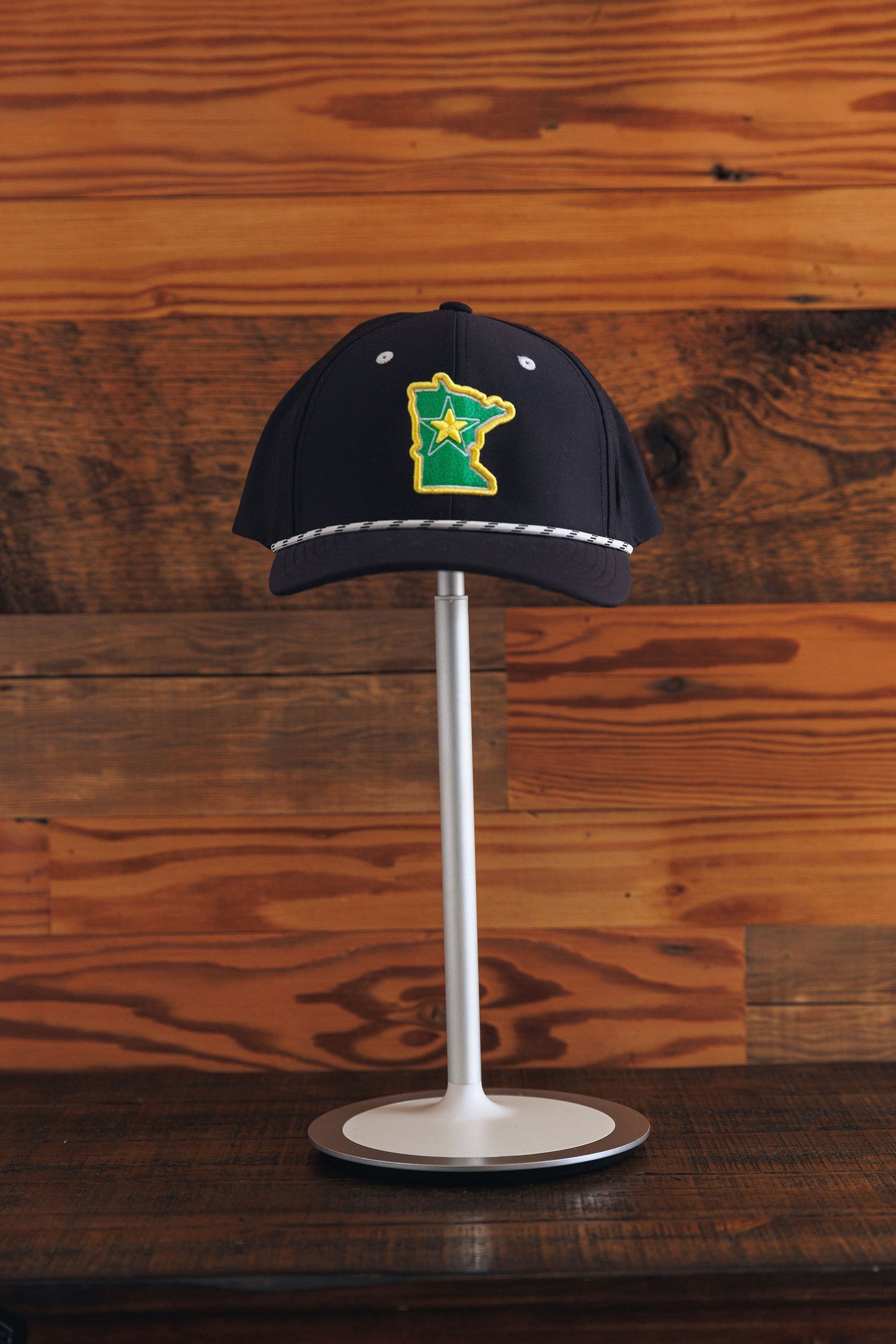 Black cap with a green and yellow design on a stand against a wooden background