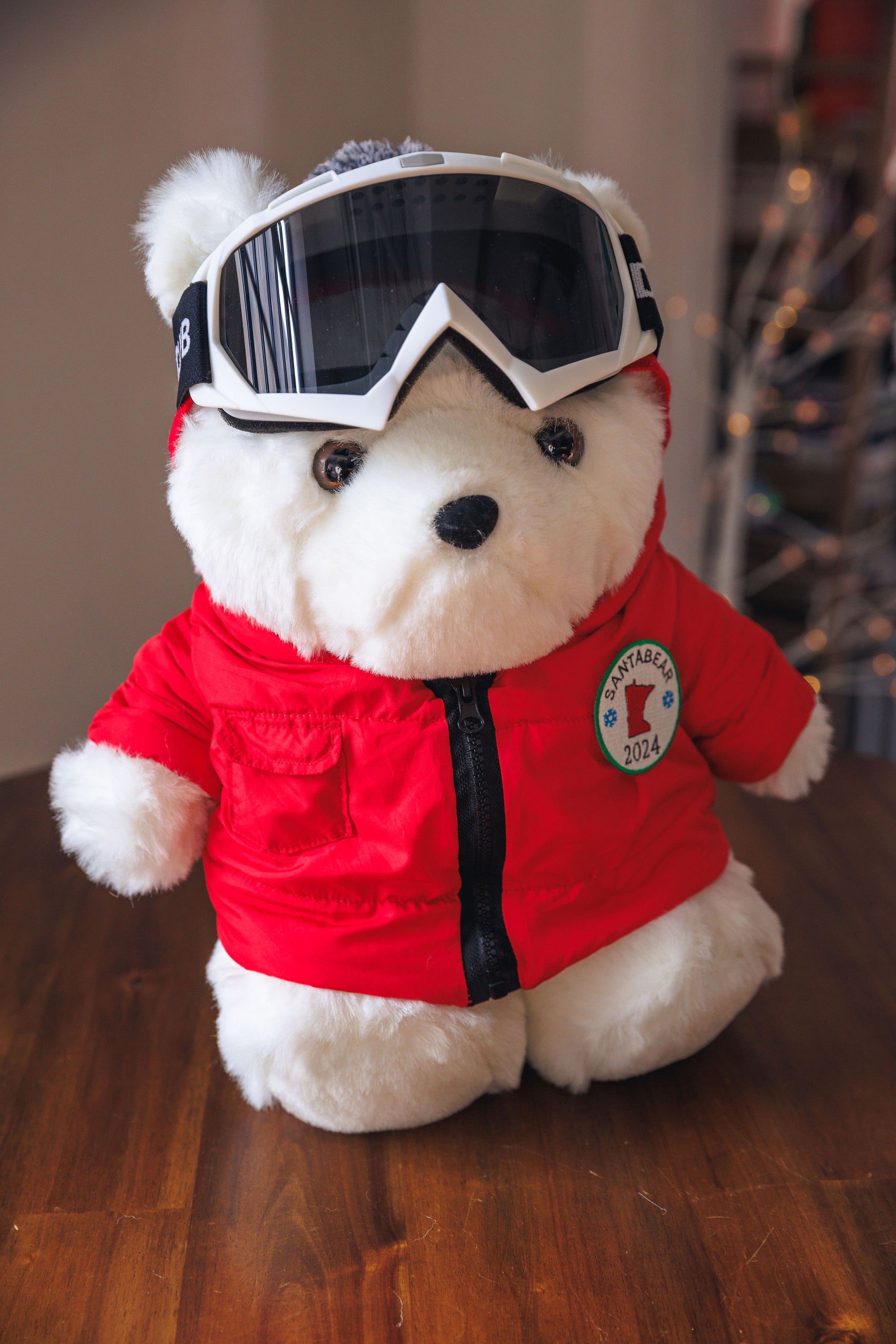 White teddy bear wearing a red jacket and goggles on a wooden surface.