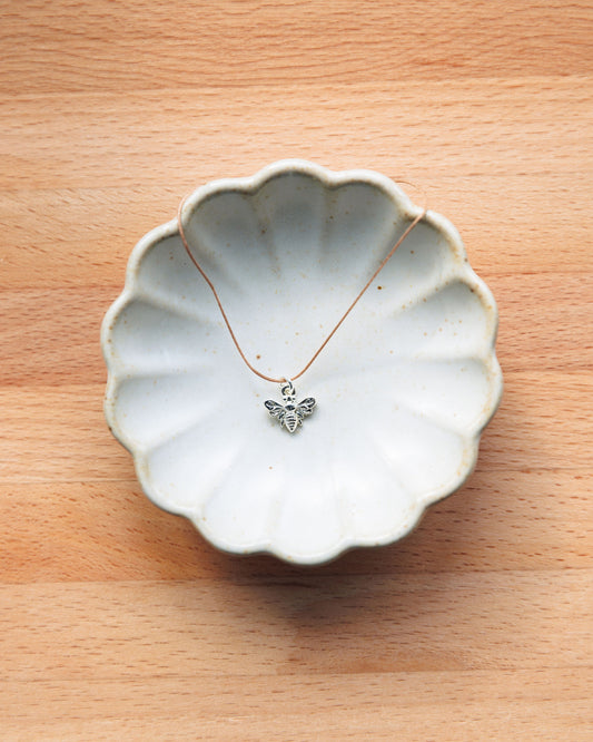 Necklace with a bee pendant on a ceramic dish on a wooden surface