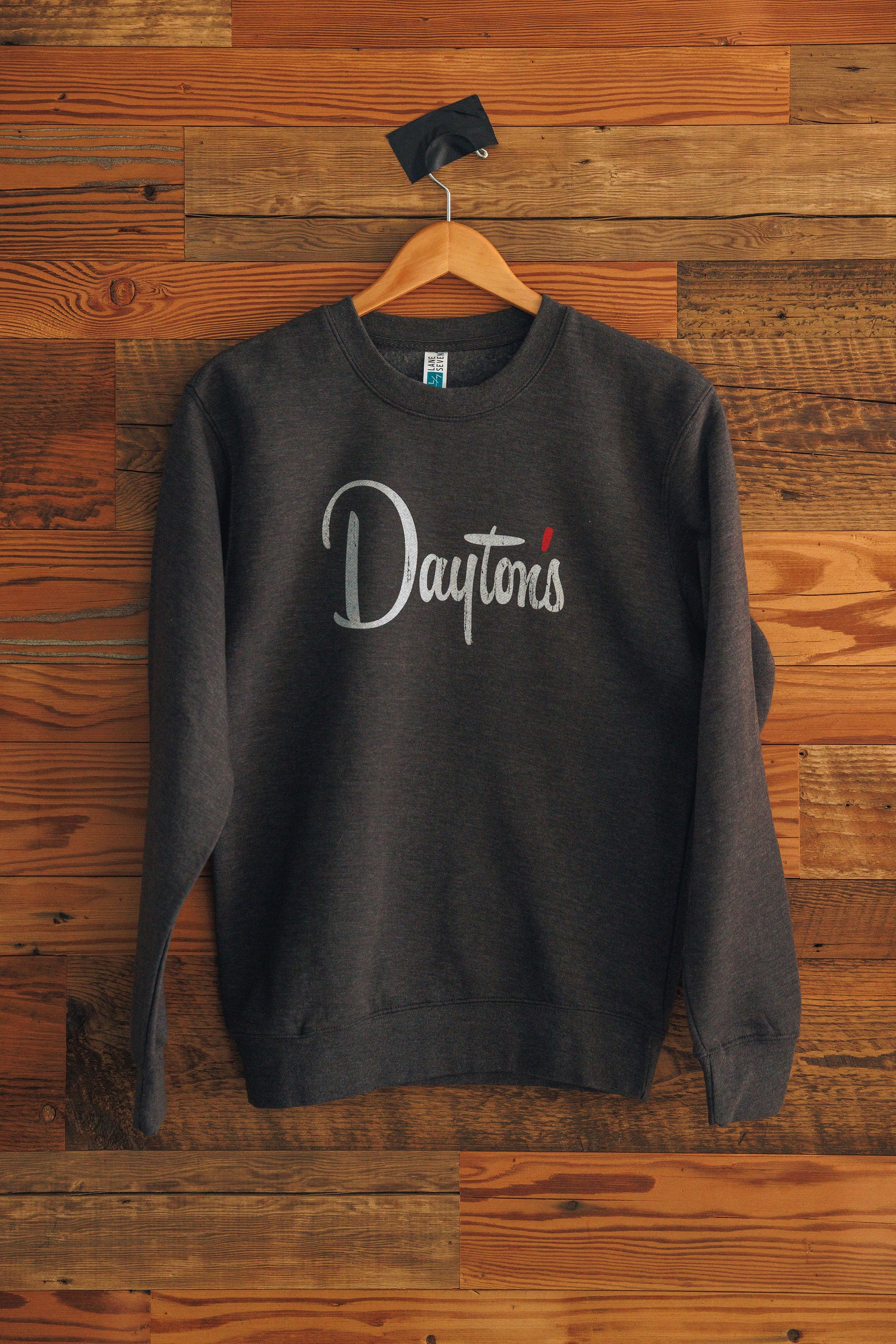 Dark gray sweatshirt with 'Dayton's' logo on a wooden hanger against a wooden wall.