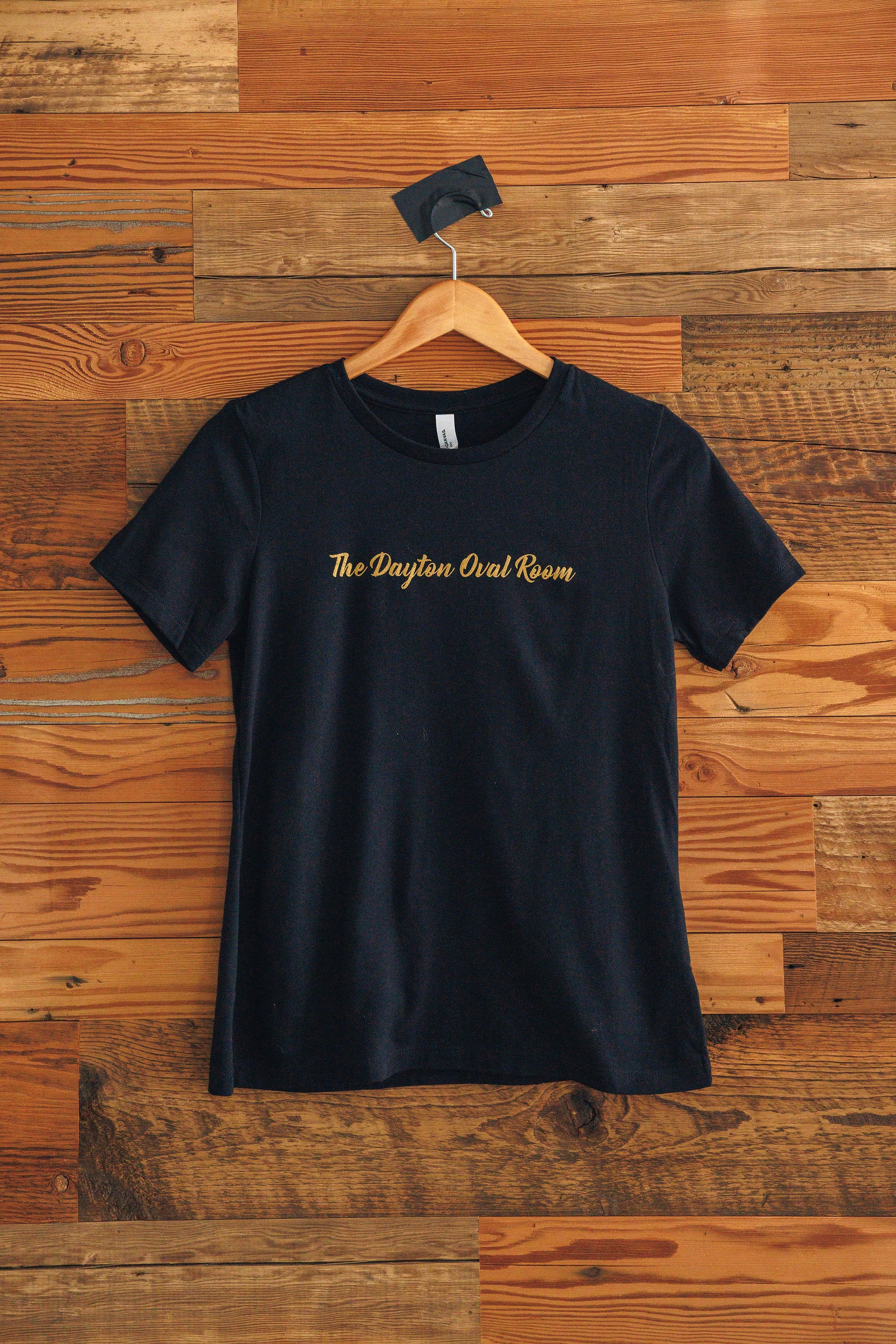 Black t-shirt with gold text on a wooden background