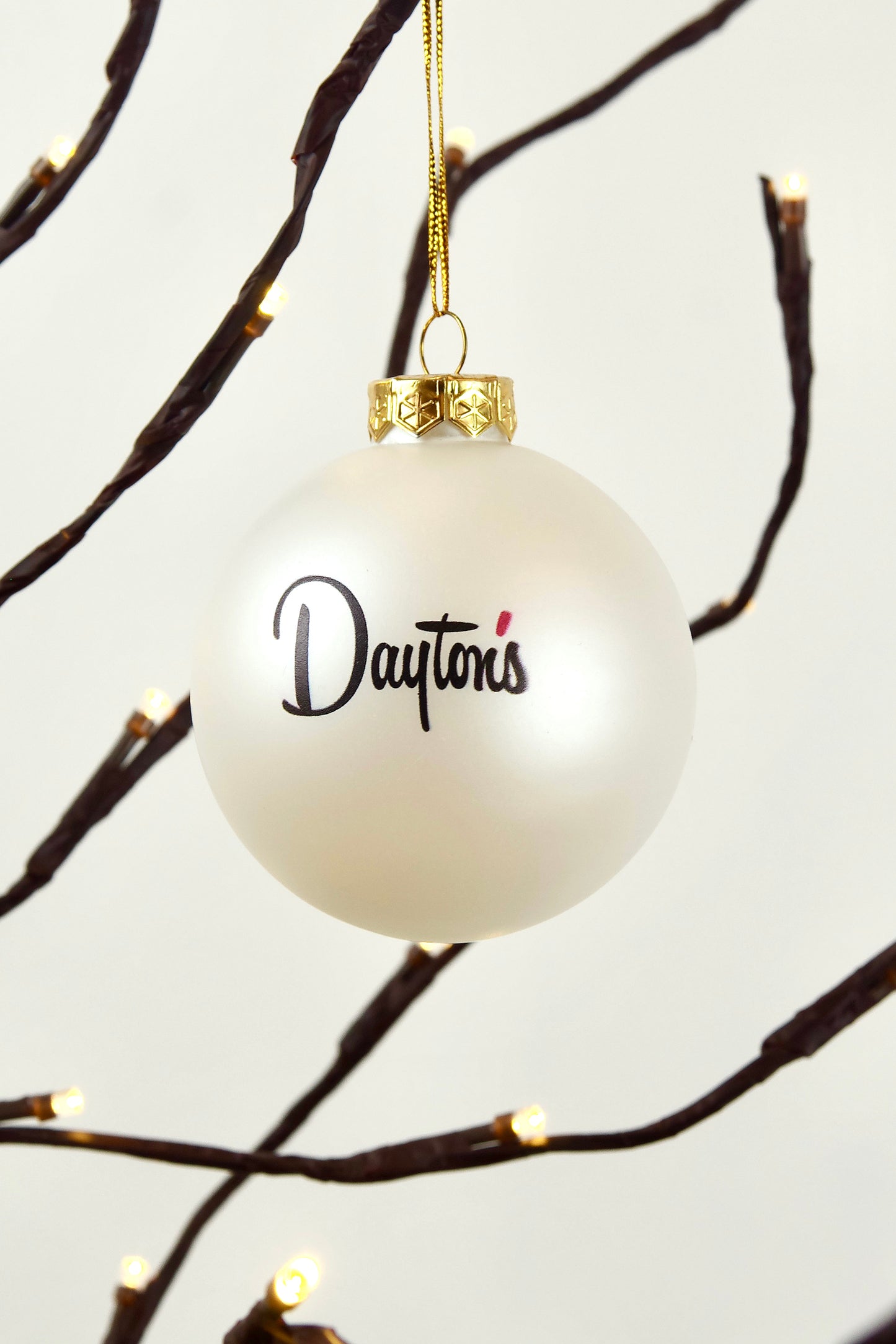 White ornament with 'Dayton's' text hanging on a branch with lights