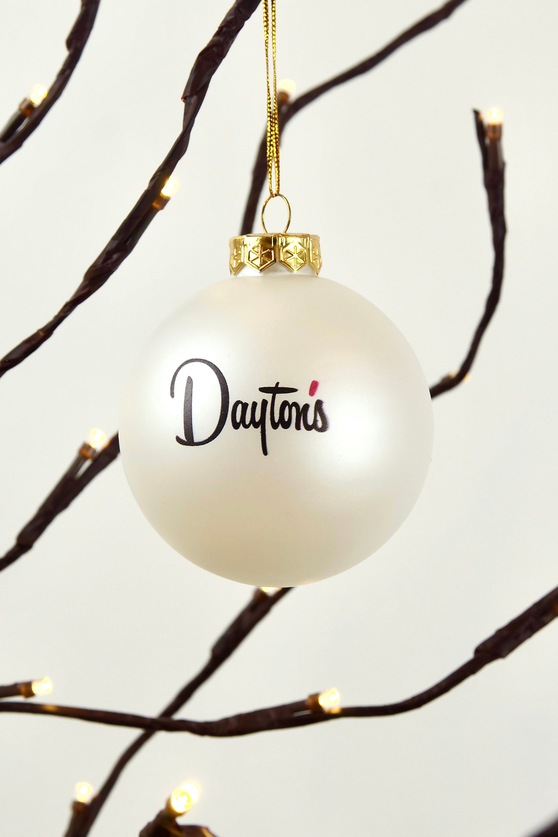 White ornament with 'Dayton's' text hanging on a branch with lights