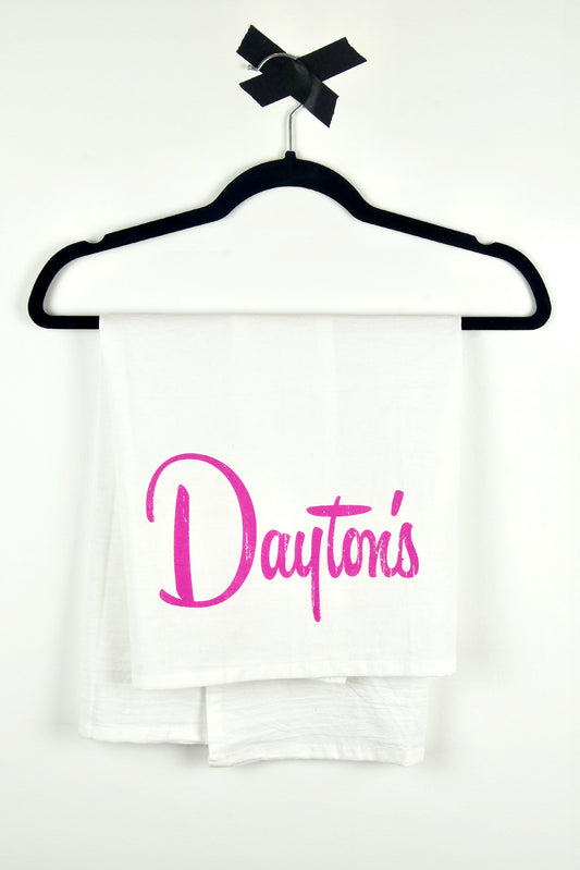 White flour sack towel with 'Dayton's' printed in pink on a black hanger against a white background