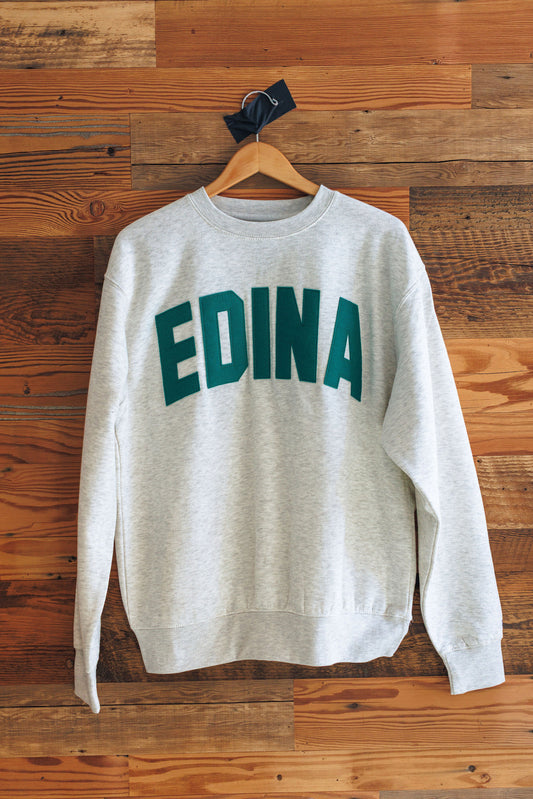 Gray sweatshirt with 'EDINA' printed in green on a wooden wall background
