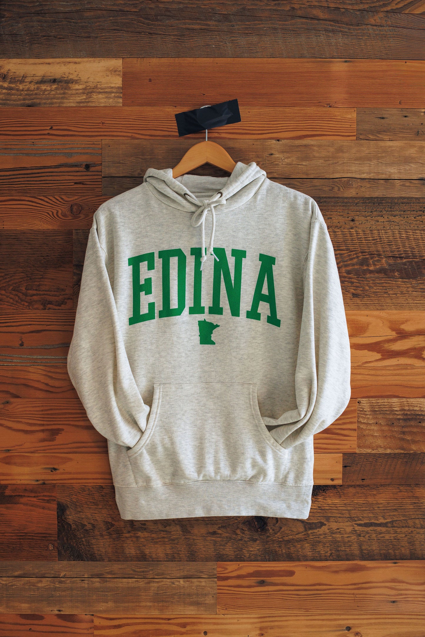 Gray hoodie with 'Edina' printed in green on a wooden background