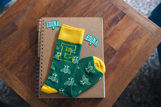Green socks with yellow accents on a notebook with 'Edina' branding on a wooden surface.