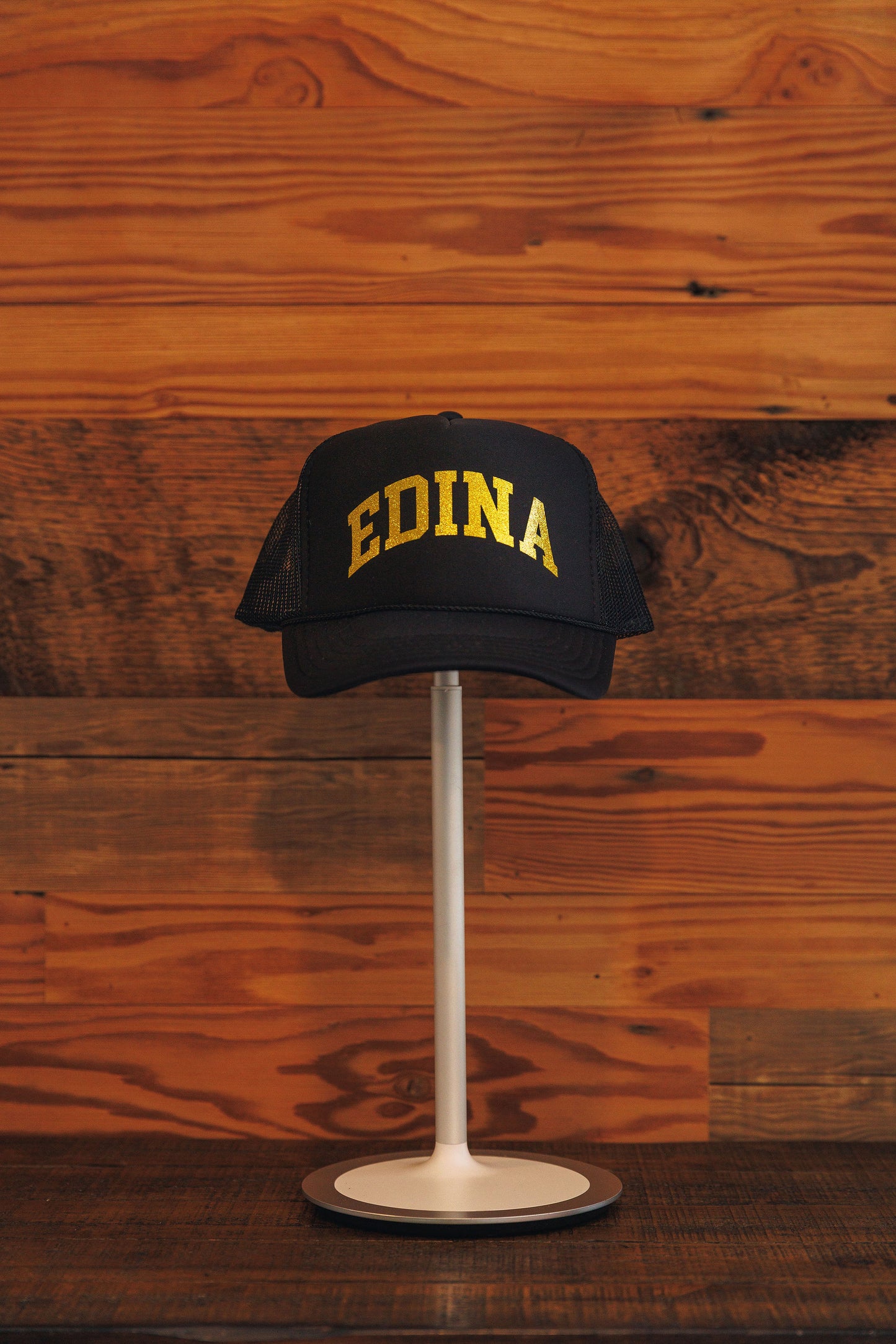Black cap with 'EDINA' text on a stand against a wooden background