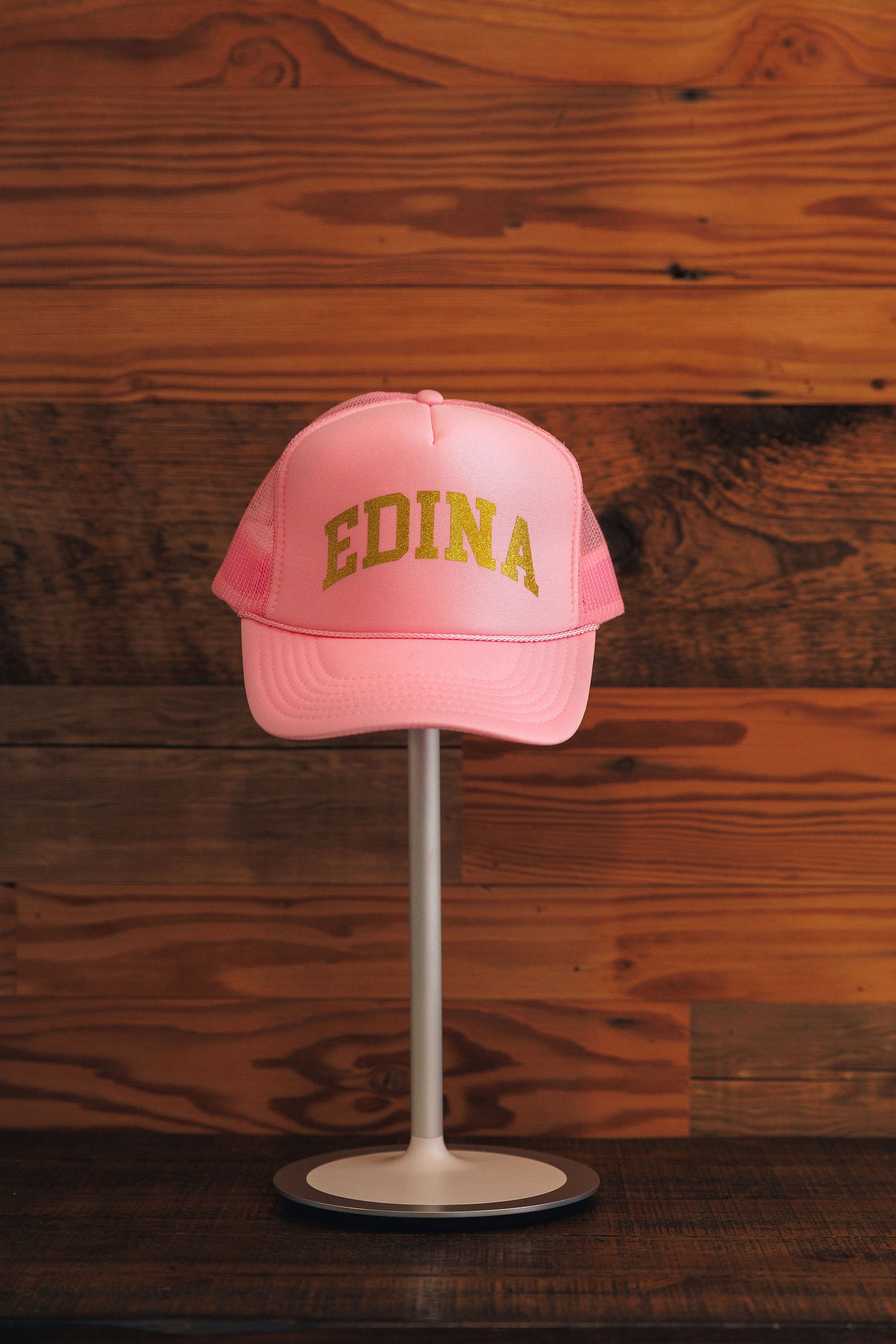 Pink cap with 'EDINA' text on a stand against a wooden background