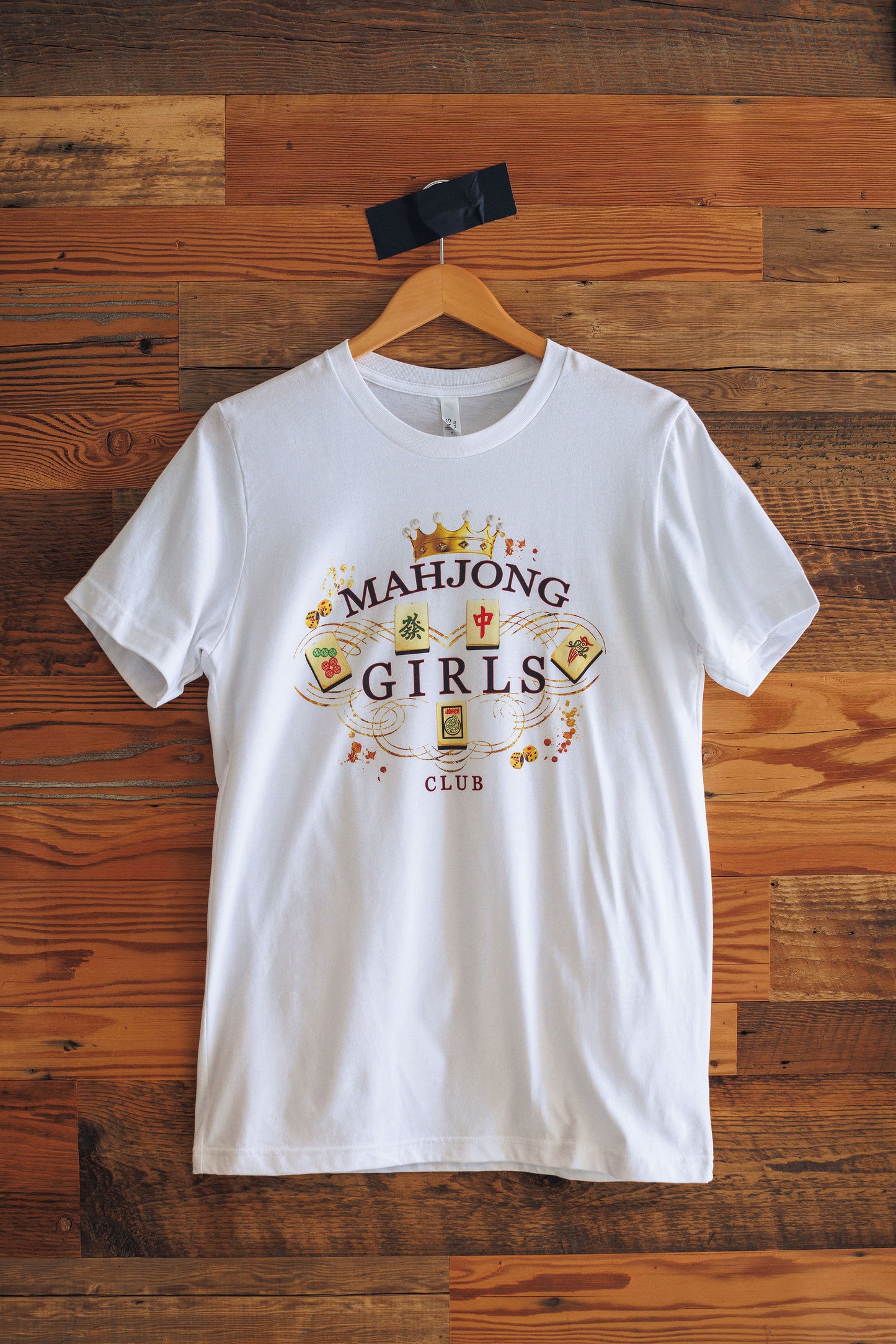 White t-shirt with 'Mahjong Girls Club' design on a wooden background