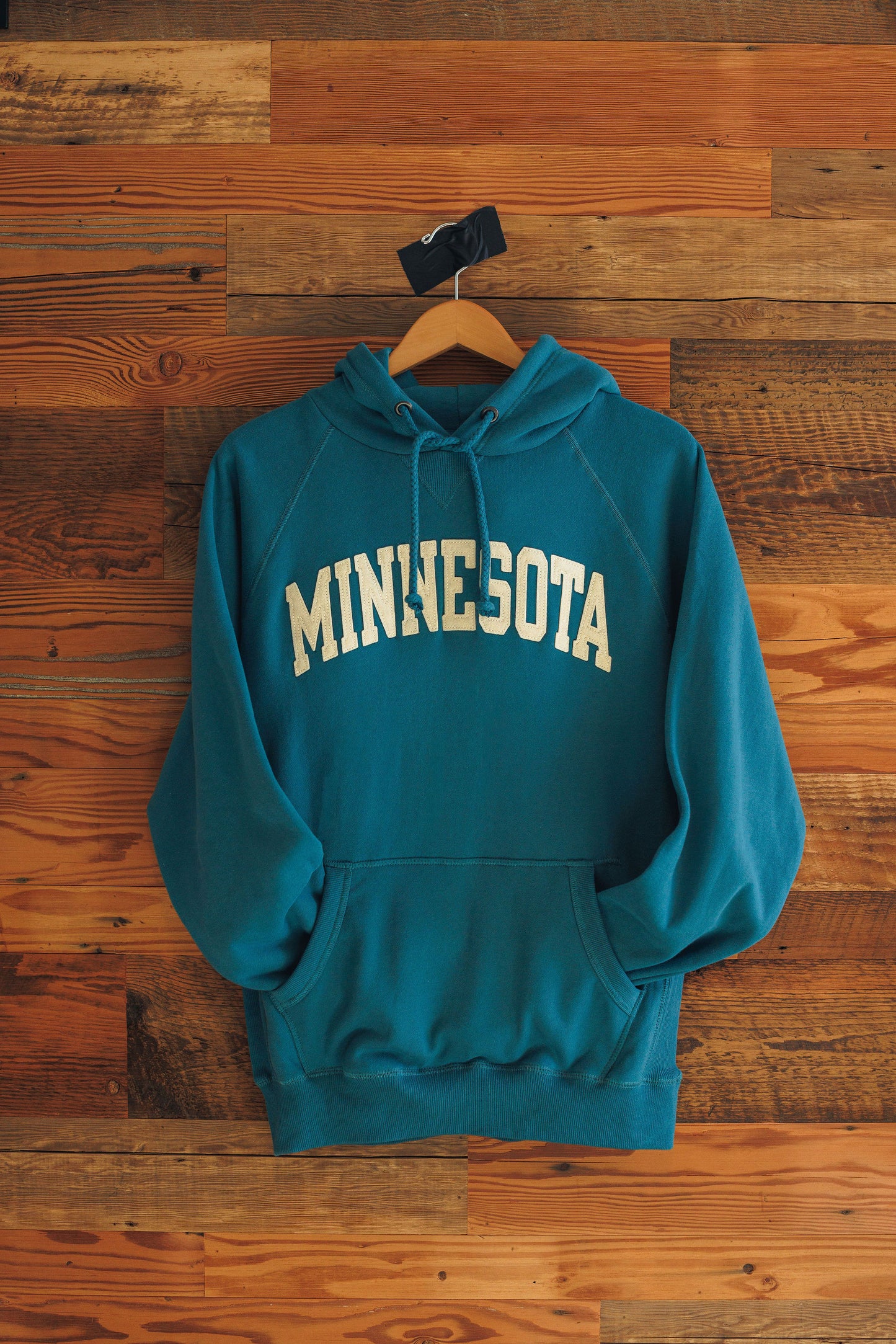 Teal hoodie with 'MINNESOTA' text on a wooden background
