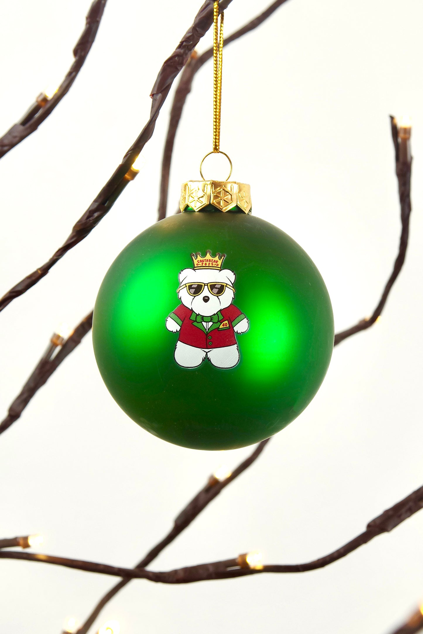 Green Christmas ornament with Santabear wearing a red coat and gold crown, hanging against a branch background.