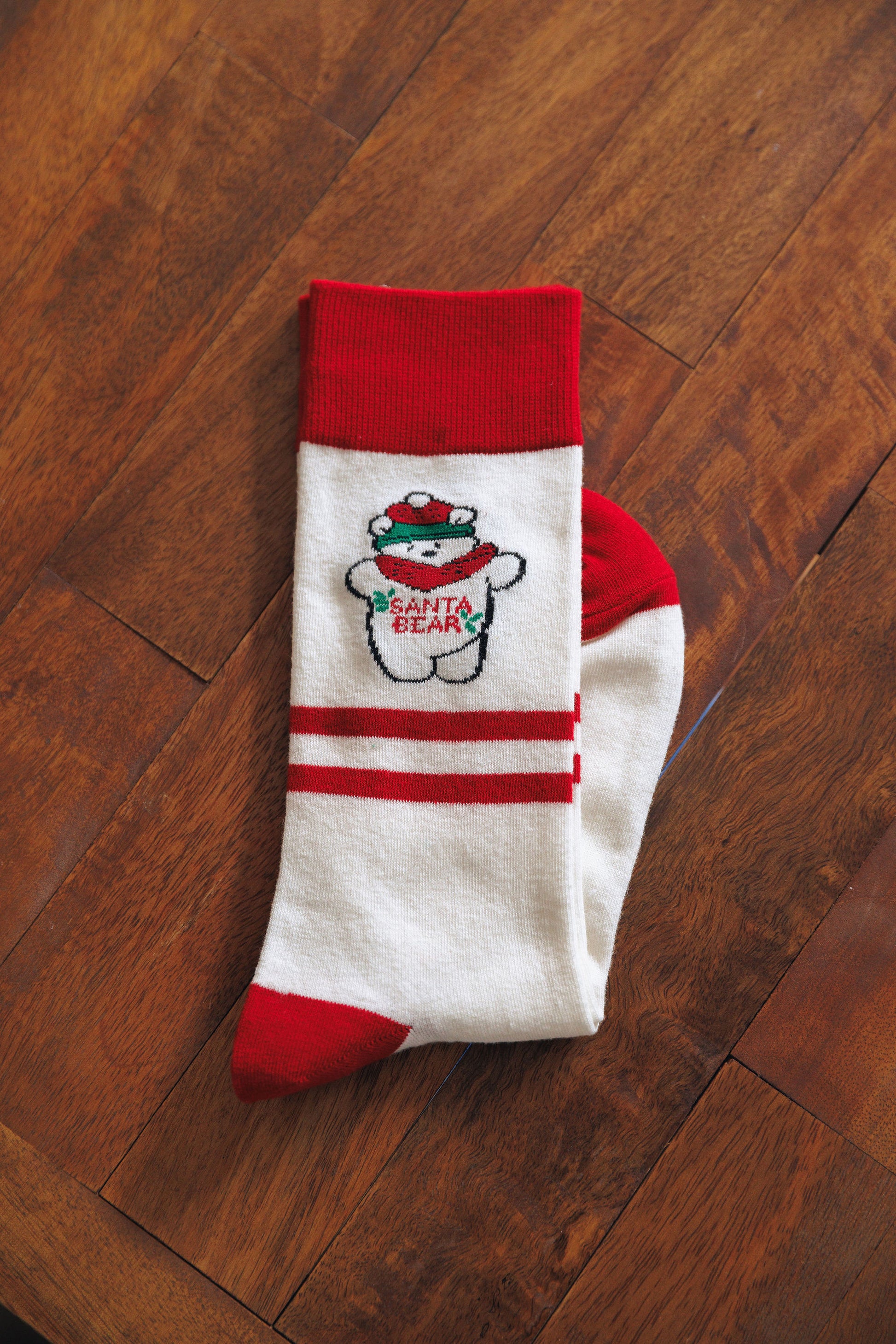 Red and white sock with cartoon Santabear design on a wooden floor