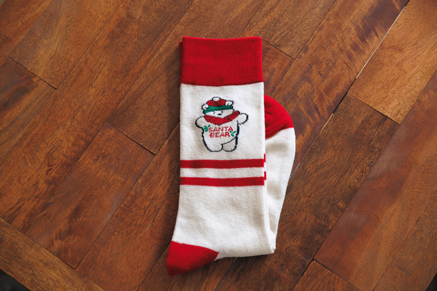 White sock with red accents featuring a Santabear design on a wooden floor