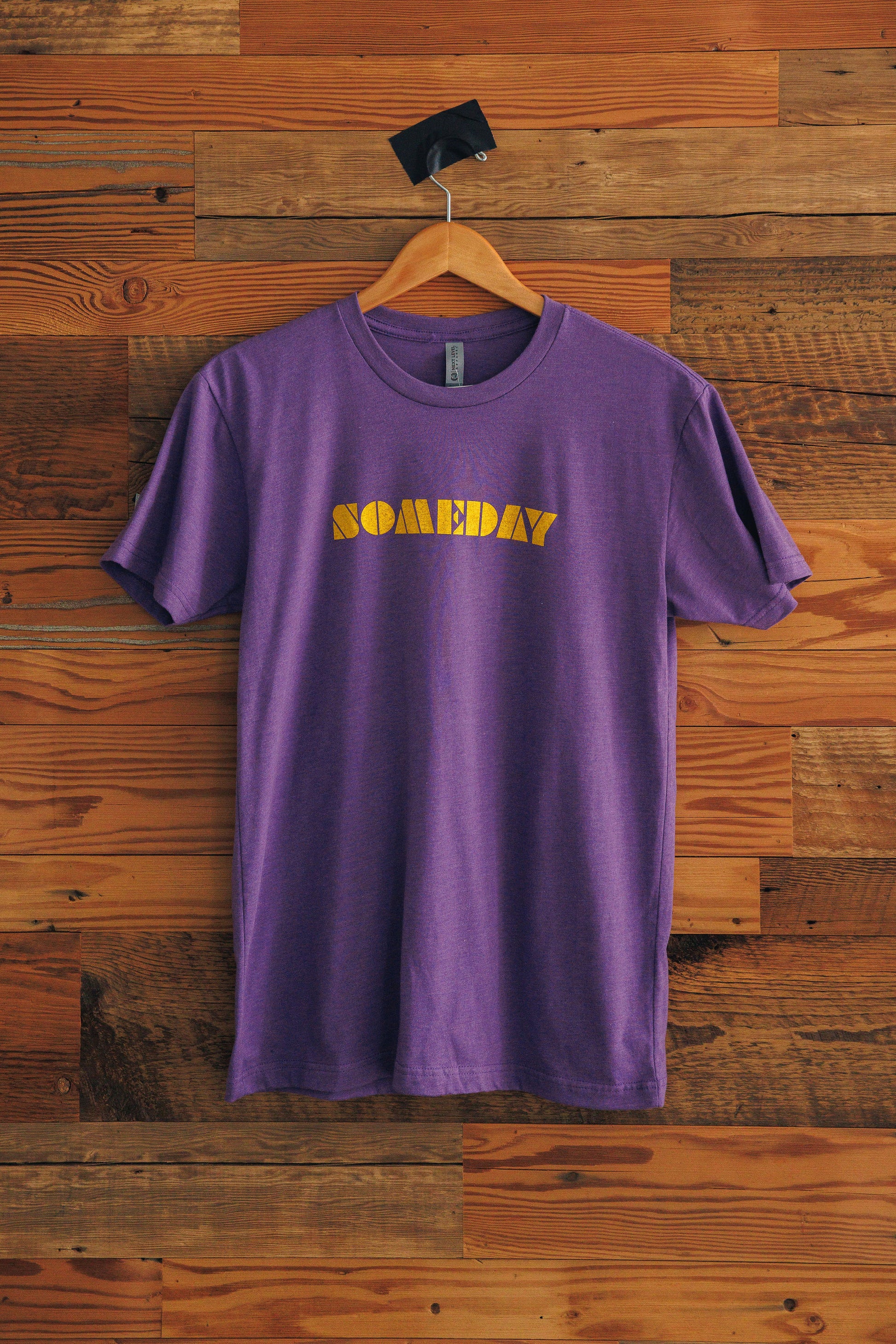 Purple t-shirt with 'SOMEDAY' text on a wooden background