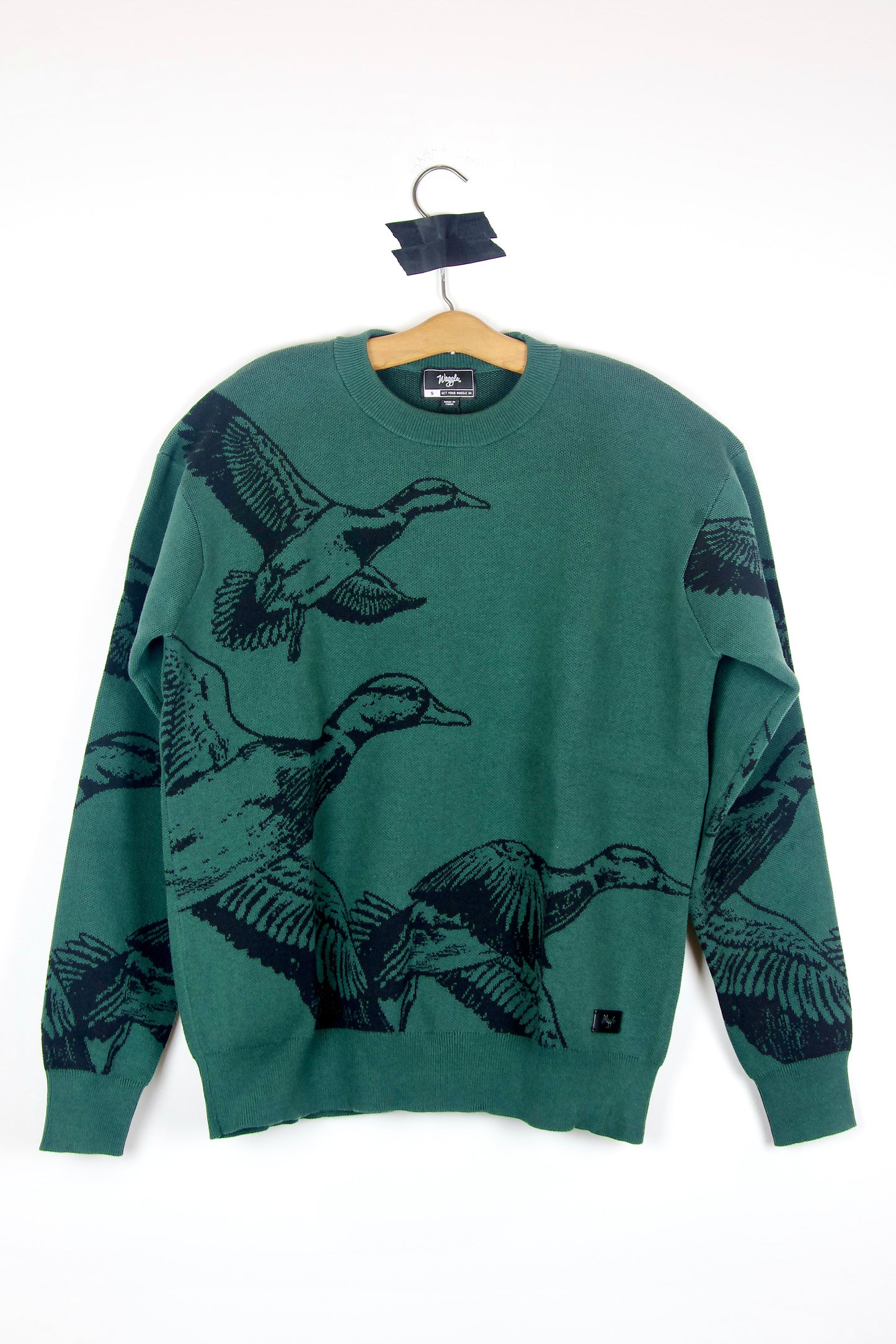 Green sweater with duck designs on a hanger against a white background
