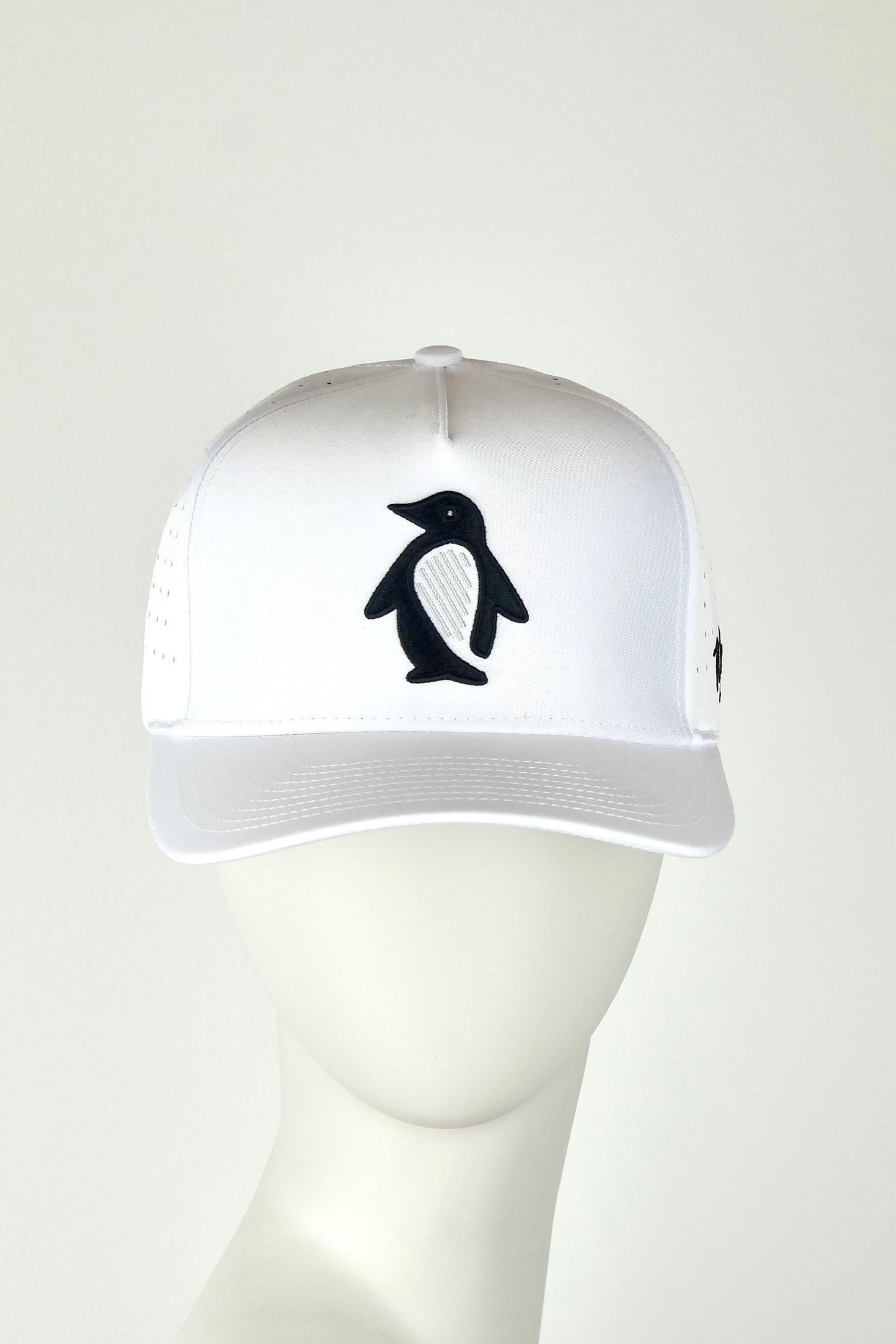 White cap with a black penguin design on a mannequin head against a white background