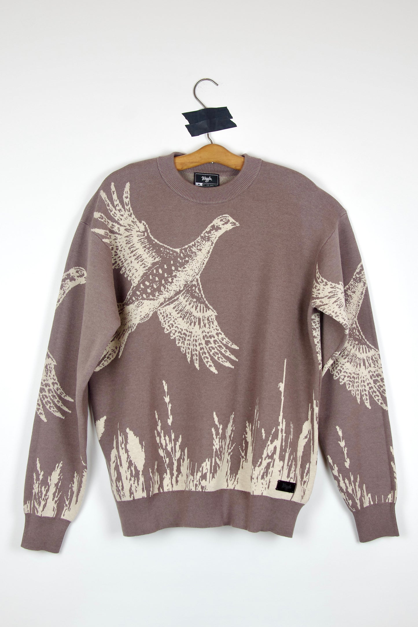 Brown sweater with pheasant and grass pattern on a hanger against a white background