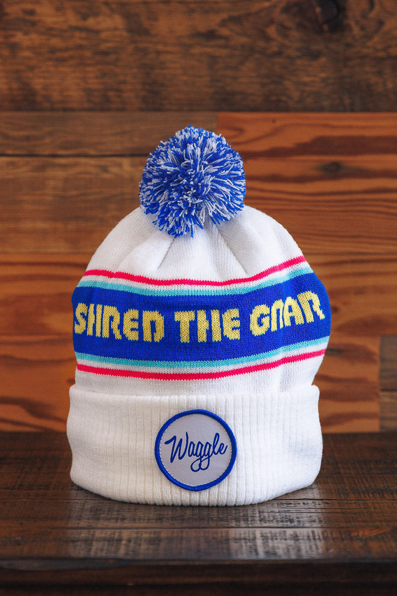 White beanie with colorful stripes and pom-pom on a wooden surface
