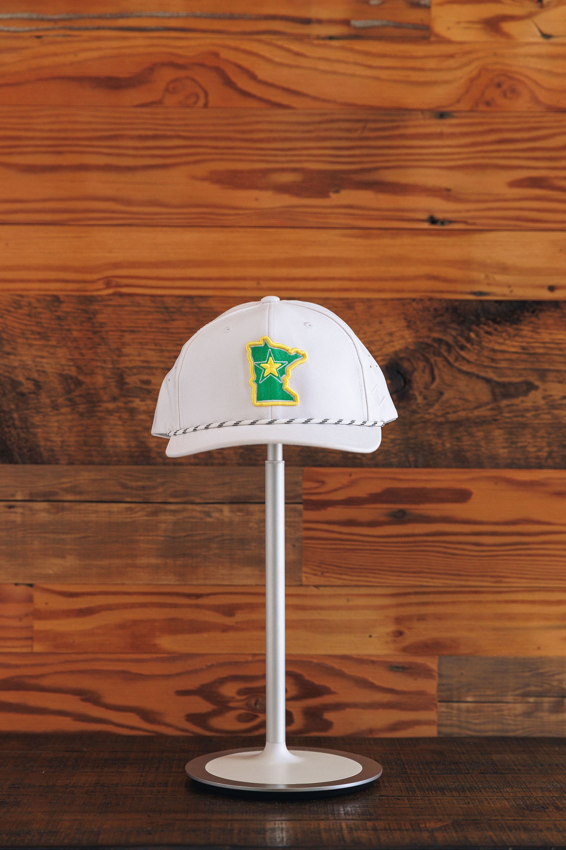 White cap with a green and yellow logo on a stand against a wooden background