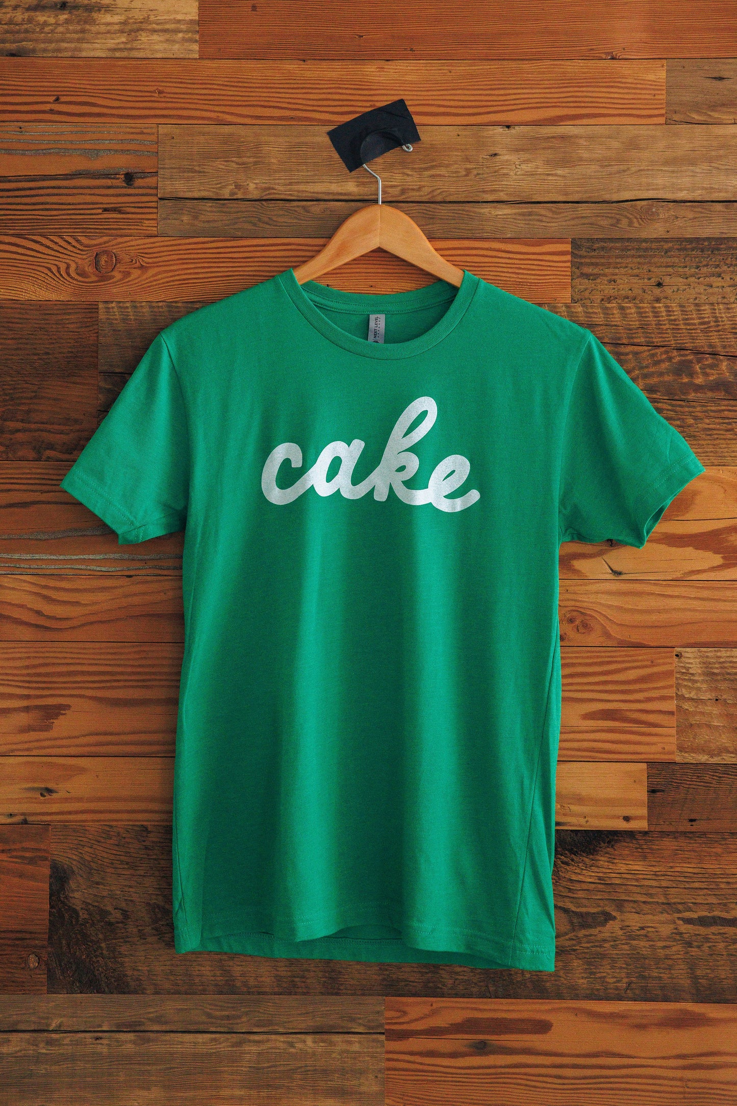 Green t-shirt with 'cake' in cursive text on a wooden background