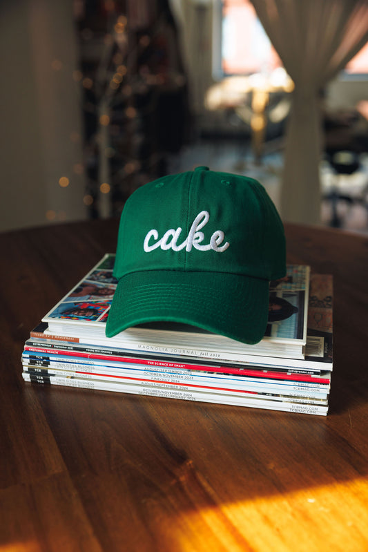 Green cap with 'cake' text on a stack of magazines on a wooden table